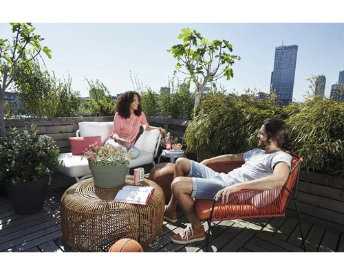 Ontspannen dakterras met loungemeubels, een rotan tafel en diverse potplanten tegen de achtergrond van een skyline.