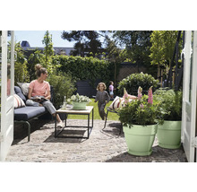 Modern ingericht terras met bestrating, tuinmeubelen, salontafel en plantenpotten met spelende kinderen op het gazon op de achtergrond.