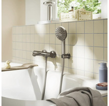 Metalen badmengkraan met handdouche aan een betegelde wand boven een badkuip in een lichte, georganiseerde badkamer.