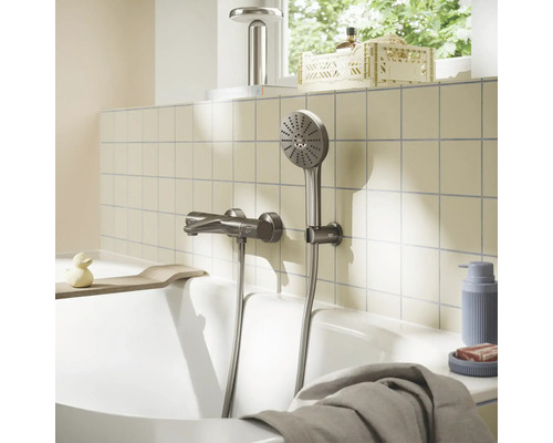 Metalen badmengkraan met handdouche aan een betegelde wand boven een badkuip in een lichte, georganiseerde badkamer.