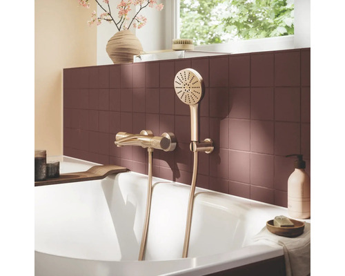 Badmengkraan en handdouche in goudlook op een rood betegelde muur boven een wit bad in een lichte badkamer.