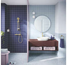 Moderne badkamer met vierkante wandtegels, doucheruimte met gouden kraan, wastafelmeubel met opzetwastafel, ronde spiegel en terrazzovloer.