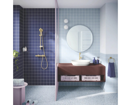 Moderne badkamer met vierkante wandtegels, doucheruimte met gouden kraan, wastafelmeubel met opzetwastafel, ronde spiegel en terrazzovloer.