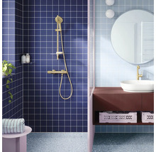 Moderne badkamer met blauwe vierkante tegels, gouden douchesysteem, witte opzetwastafel op een bruin wastafelmeubel en een ronde spiegel.