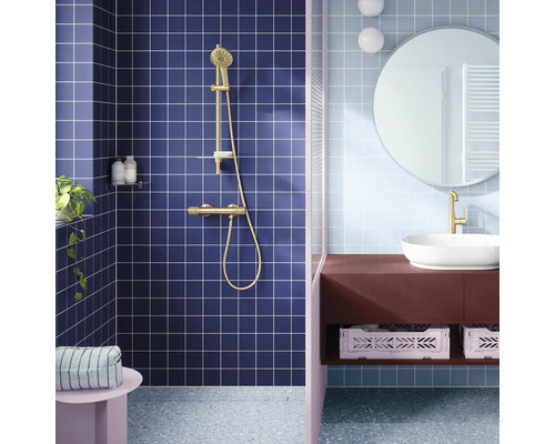 Moderne badkamer met blauwe vierkante tegels, gouden douchesysteem, witte opzetwastafel op een bruin wastafelmeubel en een ronde spiegel.