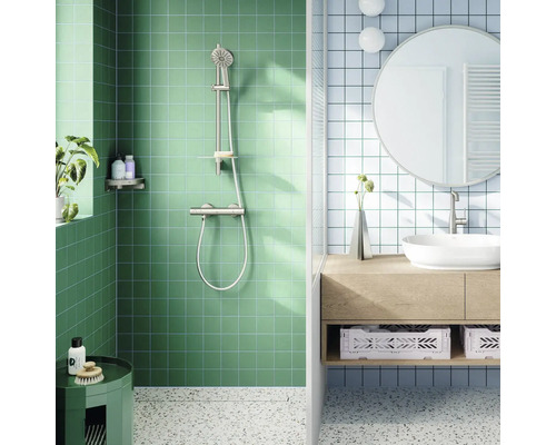 Moderne lichte badkamer met groene douche en metalen doucheset. Blauwe tegels, houten meubel, witte opzetwastafel, ronde spiegel en terrazzovloer.