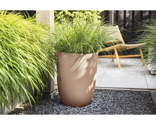 Beige plantenbak met golfstructuur en siergras op een modern terras met grijs grind.