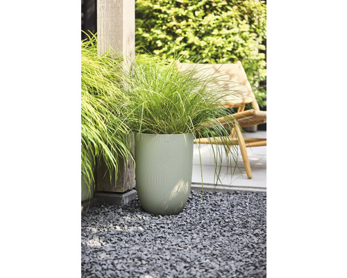 Hoge, lichtgroene plantenpot met golfstructuur en siergras op grijs grind in de tuin.