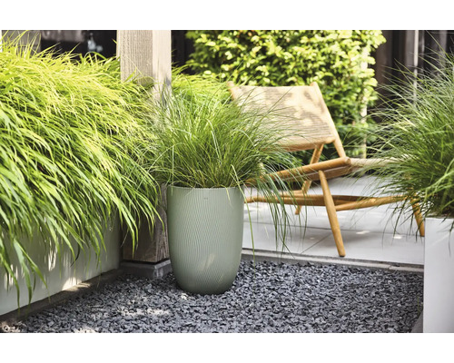 Siergras in een hoge, getextureerde groene bloempot op een modern terras met grijs split en een houten ligstoel.