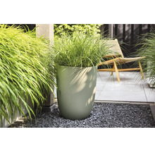 Moderne hoge plantenbak met verticale golfstructuur en siergras op een licht, georganiseerd terras met grind en tegels.