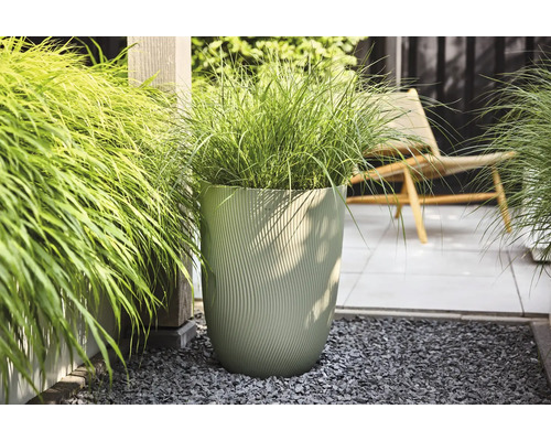 Moderne hoge plantenbak met verticale golfstructuur en siergras op een licht, georganiseerd terras met grind en tegels.