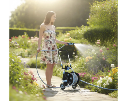 Vrouw besproeit een bloeiende tuin met een tuinslang op een slangenwagen op een licht tuinpad.