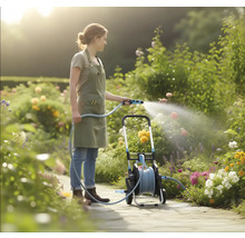 Een vrouw in een lichte tuin besproeit bloemen met een tuinslang vanaf een mobiele slangenwagen op een geplaveid pad.