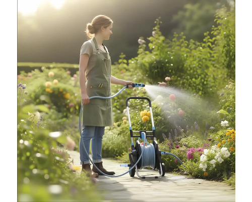 Een vrouw in een lichte tuin besproeit bloemen met een tuinslang vanaf een mobiele slangenwagen op een geplaveid pad.