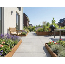 Modern licht terras met lichtgrijze tegels, houten bank, plantenbakken van cortenstaal en een zwarte kamado-barbecue.