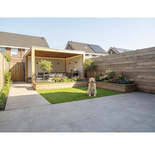 Moderne tuin met houten overkapping, zithoek, barbecue, houten plantenbakken, kunstgras, grijze terrastegels en een schutting.