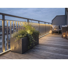Verlicht dakterras met houten terrasplanken, metalen reling met LED-strips, grote plantenbak en loungebank in de avond.