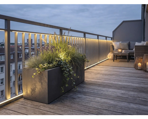 Verlicht dakterras met houten terrasplanken, metalen reling met LED-strips, grote plantenbak en loungebank in de avond.