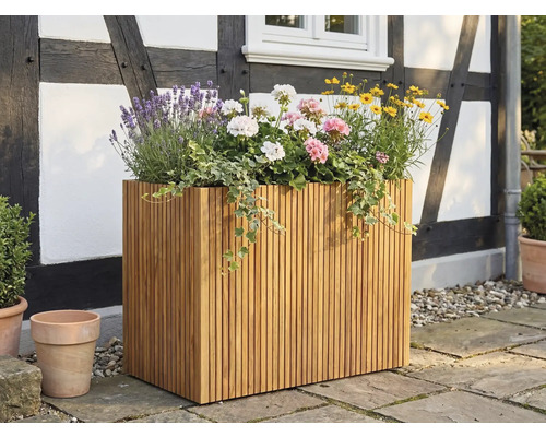 Grote rechthoekige plantenbak van houten latten, beplant met lavendel en geraniums, op een terras voor een vakwerkgevel.