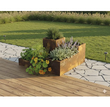 Modulaire verhoogde plantenbak van cortenstaal in een tuin met planten, naast een houten terras en een stenen pad.