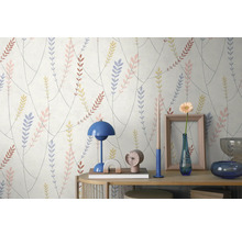 Behang met een patroon van takken en gekleurde bladeren achter een consoletafel met een lamp, vaas en decoratieve voorwerpen.