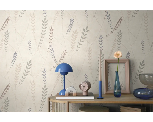 Vliesbehang met fijn bladpatroon op een lichte achtergrond boven een dressoir met tafellamp en decoratie.