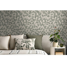 Vliesbehang met botanisch bladerpatroon in een slaapkamer achter een bed met kussens en een kamerplant op een bijzettafel.