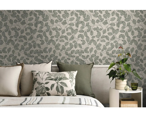 Vliesbehang met botanisch bladerpatroon in een slaapkamer achter een bed met kussens en een kamerplant op een bijzettafel.