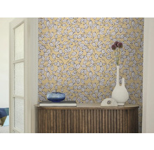 Woonkamer met behang met bladpatroon, een houten dressoir, een witte vaas en een blauwe glazen schaal.