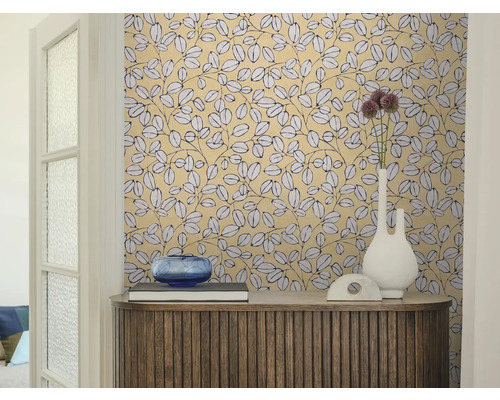 Woonkamer met behang met bladpatroon, een houten dressoir, een witte vaas en een blauwe glazen schaal.
