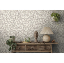 Behang met bladerpatroon in een lichte kamer. Een houten sidetable is versierd met een tafellamp, een stenen beeld en planten.