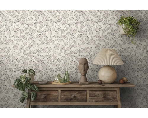 Behang met bladerpatroon in een lichte kamer. Een houten sidetable is versierd met een tafellamp, een stenen beeld en planten.
