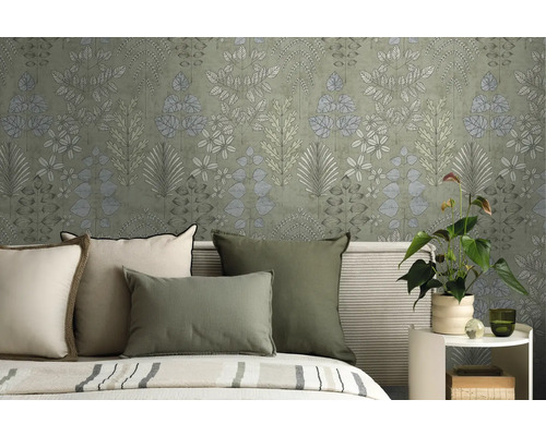 Vliesbehang met botanisch bladerpatroon in een slaapkamer achter een bed met groene en crèmekleurige kussens.
