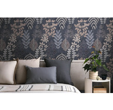 Vliesbehang met botanisch bladerpatroon in donkerblauw en grijs achter een bed met kussens en een kamerplant op een bijzettafel.