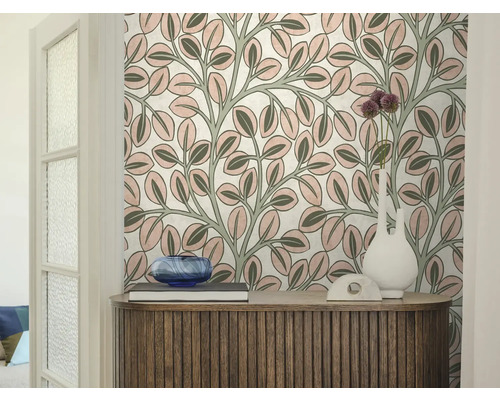 Vliesbehang met een bladerpatroon achter een houten dressoir met decoratie en een witte vaas in een lichte kamer.