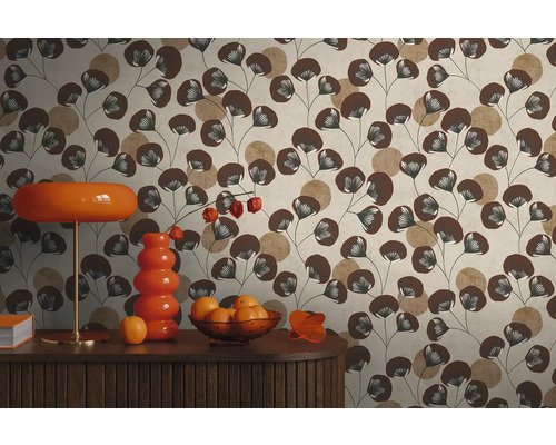 Vliesbehang met bladpatroon in bruin en beige achter een dressoir met oranje lamp en vaas in retrostijl.