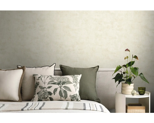 Slaapkamer met licht gestructureerd behang, sierkussens met bloemenprint en een bijzettafel met kamerplant.