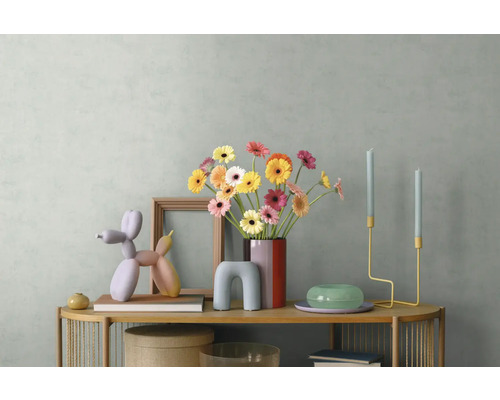Moderne dressoirdecoratie met kleurrijke gerbera's in een vaas, een ballonhondsculptuur, houten lijst en minimalistische kandelaars.