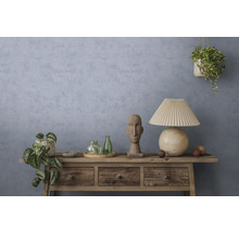 Rustiek houten dressoir voor een blauwgrijze muur met textuur, voorzien van een tafellamp, stenen sculptuur, glazen flessen en kamerplanten.