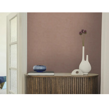Gestructureerd vliesbehang in oudroze op een muur achter een houten dressoir met latten, een witte vaas en een blauwe glazen schaal.