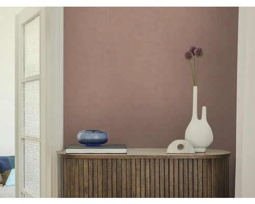Gestructureerd vliesbehang in oudroze op een muur achter een houten dressoir met latten, een witte vaas en een blauwe glazen schaal.