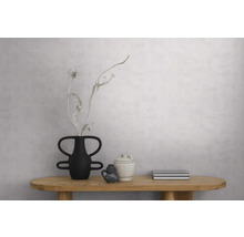 Lichtgrijs gestructureerd behang met betonlook op een muur in een minimalistische kamer met houten tafel en decoratie.