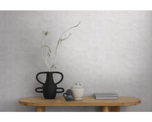 Lichtgrijs gestructureerd behang met betonlook op een muur in een minimalistische kamer met houten tafel en decoratie.
