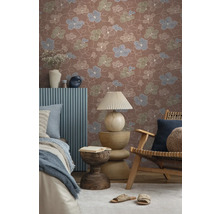 Vliesbehang met bloemenpatroon in terracotta, blauw en groen in een sfeervolle kamer met houten meubels en textiel.