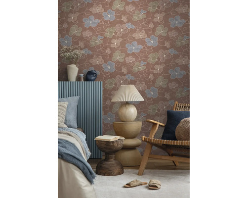 Vliesbehang met bloemenpatroon in terracotta, blauw en groen in een sfeervolle kamer met houten meubels en textiel.