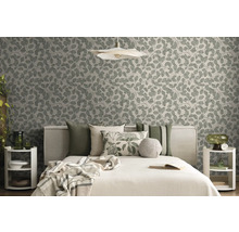Moderne slaapkamer met vliesbehang met bladmotief, bed met diverse kussens en decoratieve bijzettafels in natuurtinten.