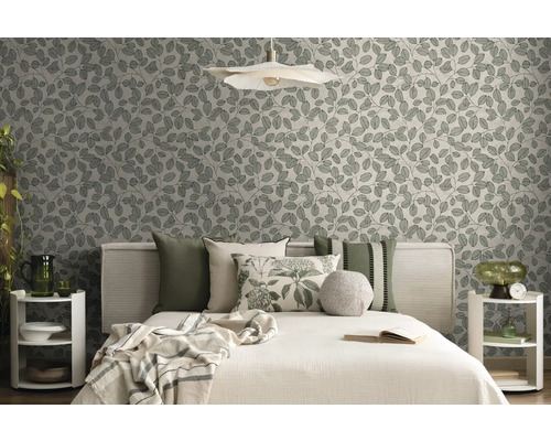 Moderne slaapkamer met vliesbehang met bladmotief, bed met diverse kussens en decoratieve bijzettafels in natuurtinten.