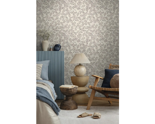 Vliesbehang met botanisch bladmotief in een lichte slaapkamer met houten fauteuil, bijzettafel en bed.