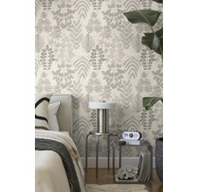 Vliesbehang met botanisch bladmotief in een lichte slaapkamer met bed, metalen tafeltjes en een grote kamerplant.