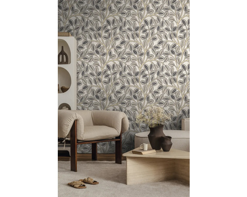 Moderne woonkamer met vliesbehang met botanisch patroon van bladeren in grijs en beige, lichte fauteuil, houten tafel en witte kast.